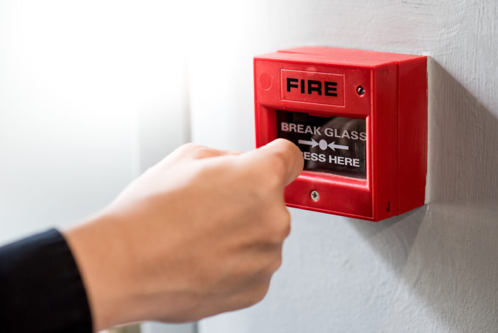 Male hand punching red fire alarm switch